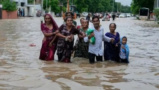 Flooding in Gujarat caused by heavy rainfall, with water reaching the first floors of houses in affected cities, and rescue operations in progress to evacuate residents.