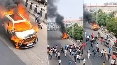 A car engulfed in flames speeds down Jaipur's elevated road as onlookers watch in shock, while firefighters rush to the scene to extinguish the blaze.